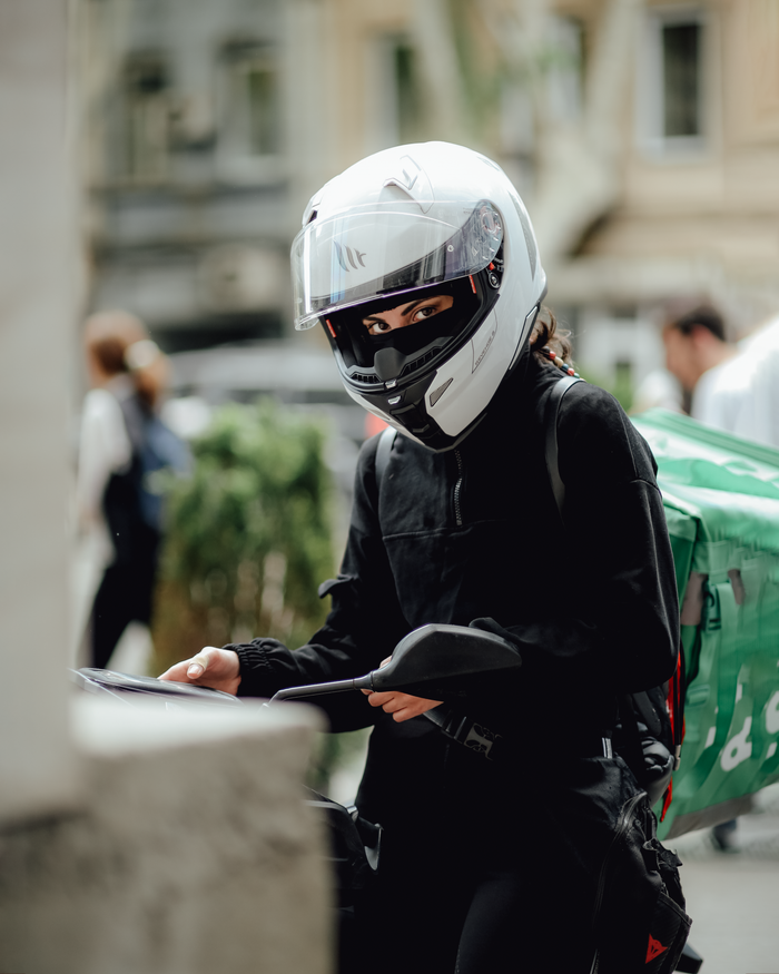 A motorcycle delivery woman in a helmet and gear checking directions in the city.